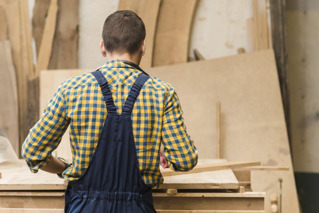 Menuisier vu de dos travaillant à son établi dans un atelier de menuiserie : santé et conditions de travail des métiers manuels