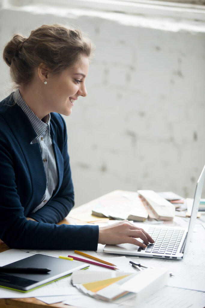 Femme souriante travaillant sur son ordinateur portable à son bureau de psychologue du travail : accompagnement des indépendants et du parcours professionnel